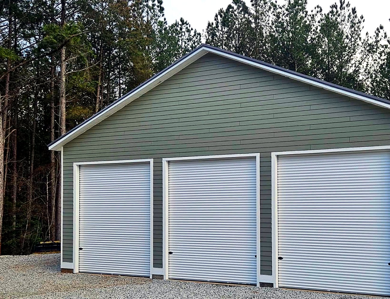 Finished three-bay detached garage with white roll-up doors and sage green siding
