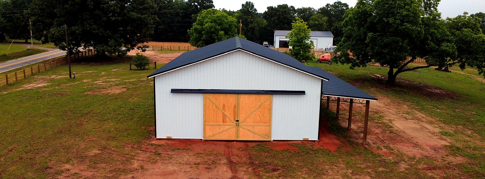 Front of a finished horse barn with wood sliding doors and a black metal roof