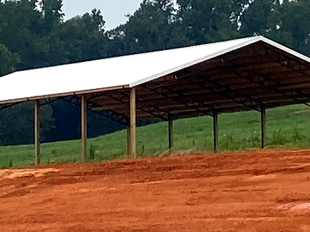 Open-sided pole barn with a white metal roof on a red clay pad